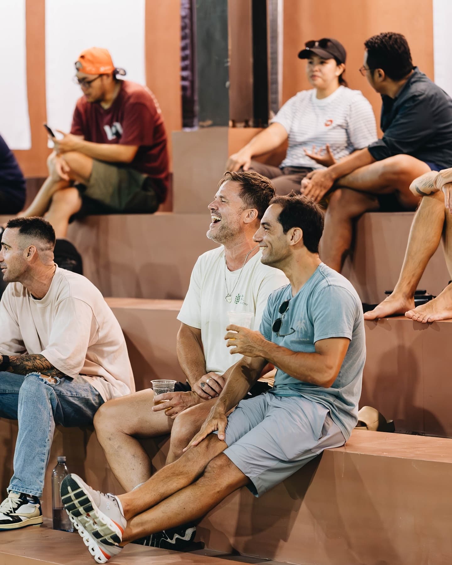 Friends laughing together on the bleachers at a social padel club